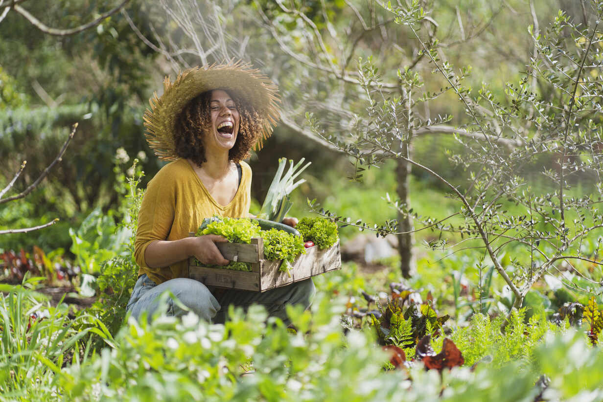 Smiling woman holding a box with freshly picked organic vegetables in natural vegetable garden